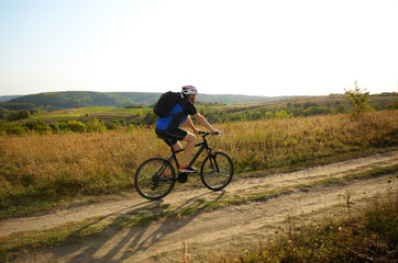 Male cyclist with backpack driving by rural dirt road outdoors