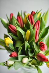 Fototapeta premium Floral background: bouquet of multicolored tulips in a glass vase on a light background, blank, mocap for mother's day greetings, international women's day