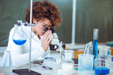 Woman scienist in laboratory. Young scientist looking through a microscope in a laboratory. Young...