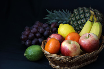 Dark Food - Chiaroscuro mixed fruit in wicker basket with dark background with copy space left