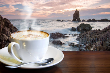Cappuccino on the table with blur landscape of sea at sunrise in the morning