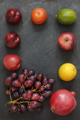 Dark Food - Chiaroscuro grapes, pomegranite, lemon, apple, lime, tangerine and plums on slate backgorund in a border with copy space in the center