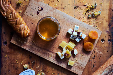 An open glass jar with natural honey, dried apricots, 3 types of cheese, grains, dorblyu, crochet. Rustic wooden background, top down
