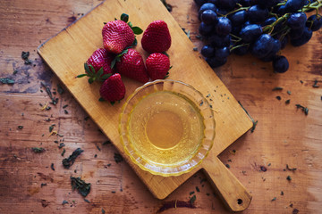 Glass plate with natural honey, blue grapes, strawberry, peach, apricot, plate of wood. Wooden background. Top down