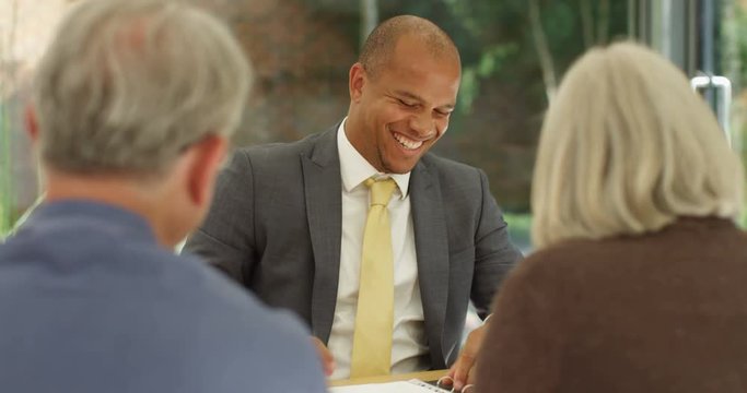 4K Happy mature couple in a meeting with bank manager, sharing a laugh & a joke