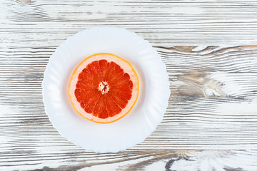 A fresh grapefruit on a white plate on a wooden background