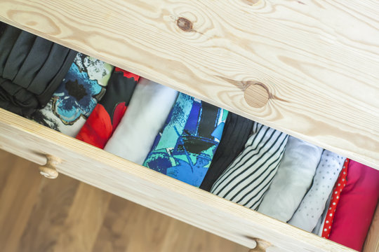 Open light wooden dresser drawer with colorful clothes.