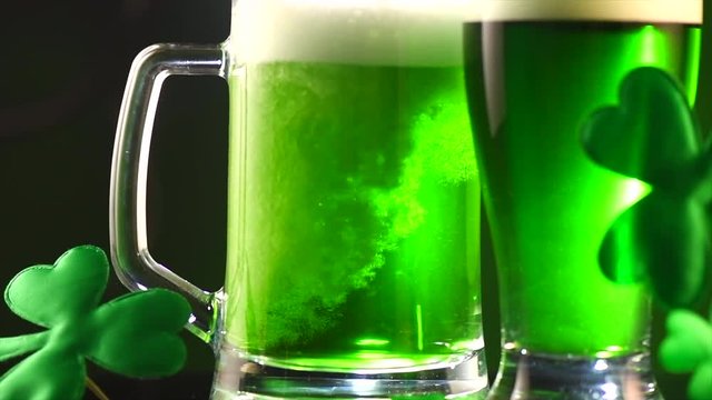 St. Patric's Day green beer pouring over deep green background, decorated with shamrock leaves. Pint of green beer closeup. 4K UHD video footage. 3840X2160