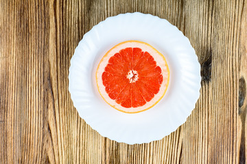 A fresh grapefruit on a white plate on a wooden background