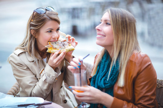 Portrait of two young women meating in cafe eating pizza outdoors,having fun together.
