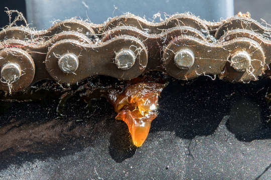 A close-up view of a chain circling the cogwheel. Part of a machine with a steel chain with greace spinning on a wheel.