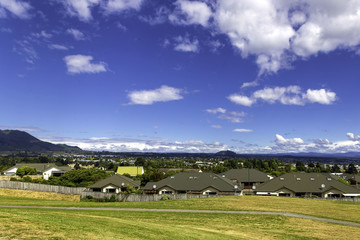 Naklejka premium Green and yellow grass lawn, roofs of the houses and the view of Taupo town in New Zealand