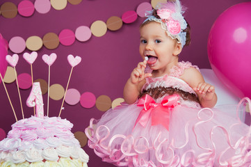 Fototapeta premium Portrait of a little cheerful birthday girl with the first cake. Eating the first cake. Smash cake