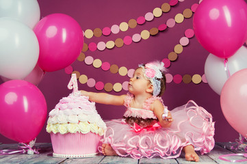 Portrait of a little cheerful birthday girl with the first cake. Eating the first cake. Smash cake
