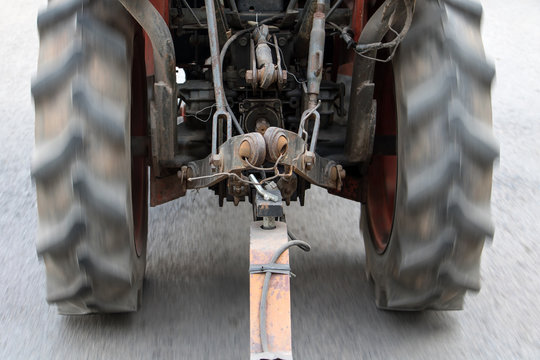 An old tractor ride on asphalt road and pulls a load with rod.