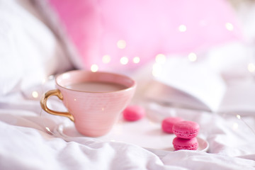 Mug with coffee and cookies staying on tray in bed with lights at background. Good morning. Selective focus.