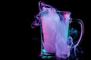 A glass transparent beer glass filled with a wig from a blue, blue, purple wipe smokes and stands on a black isolated background