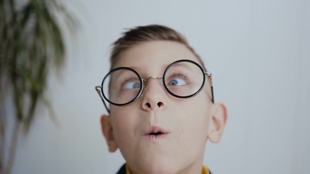 Close-up of the face of a little boy who has strabismus eyes and poor eyesight and he wears glasses to see better. The boy has blue eyes. In white background