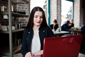Fototapeta premium Brunette girl sitting on cafe and working with red laptop.