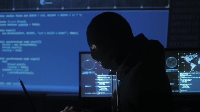 Dangerous hacker in the mask tries to enter the system using codes and numbers to find out the security password. The concept of cybercrime.
