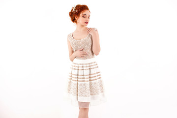 young girl with red hair in a beige lace dress standing on a white wall background