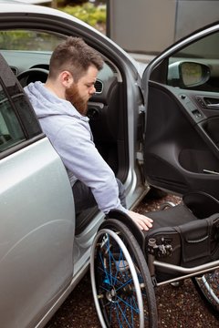 Disabled man holding wheelchair while boarding in his car