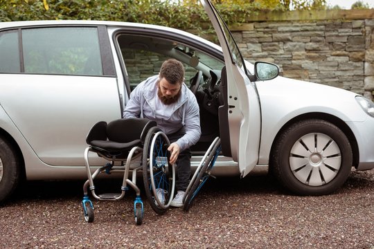 Disabled man holding wheelchair while getting out of a car