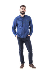 Relaxed young man wearing blue denim shirt with hands in pockets looking at camera. Full body...