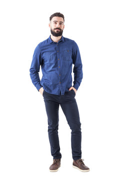 Relaxed Young Man Wearing Blue Denim Shirt With Hands In Pockets Looking At Camera. Full Body Isolated On White Background. 