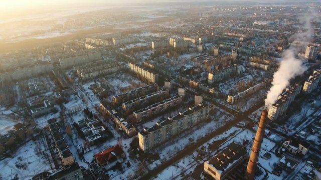 A wonderful bird`s eye view of a high cooling tube with dense swhite moke between multistoried buildings at splendid sunset in winter 
