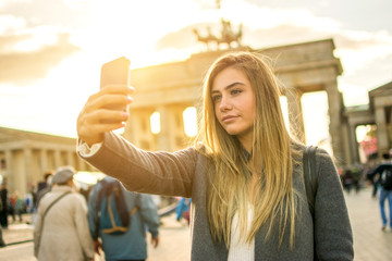 Beautiful blond young woman taking selfie in front of Brandenburg Gate in the city of Berlin,...