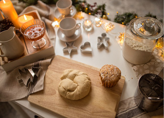 The dough for baking lies on the table with Christmas garlands and candles. Next to a plate of jam and a Cup of tea