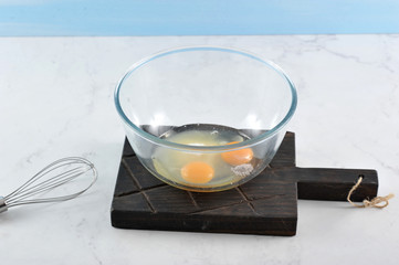 In a deep bowl, eggs, sugar, vanillin for biscuit. In the frame, a whisk for knocking. Light marble background. Close-up.