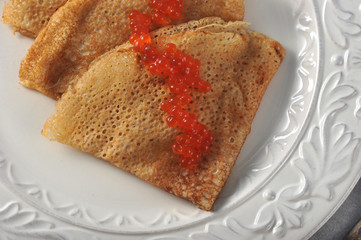 Pancakes thin on a white plate. On the pancakes is red caviar.  Light background. View from above....