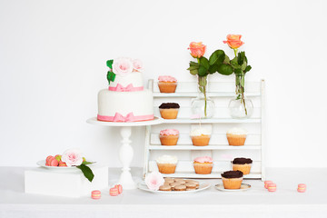 Cake decorated with roses and bows with cupcakes and macaroons standing on a table
