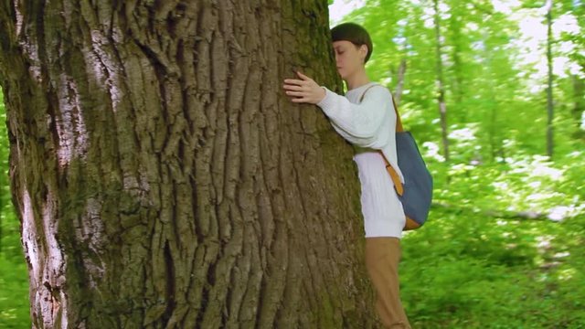 Girl hugs the big tree in the forest, love for nature. Steadicam shot, camera flying around the tree.