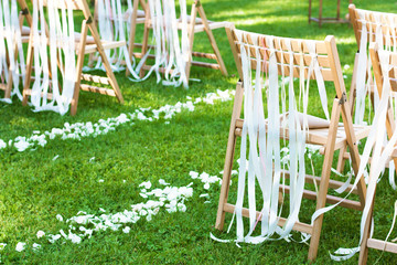 Wooden chairs decorated with bows and path of petals on wedding ceremony outdoors