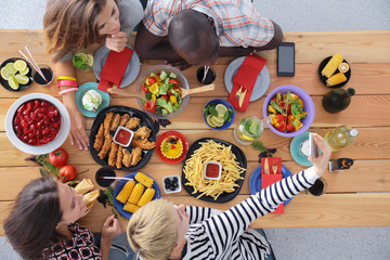 Top view of group of people having dinner together while sitting at wooden table. Food on the table. People eat fast food.