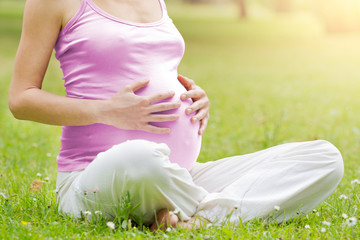 Pregnant caucasian woman holding her tummy in the park during a sunset