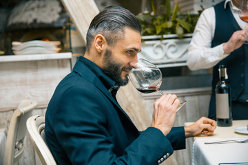 handsome bearded rich man with stylish mustache and beard holding glass and sniff smell of red wine at the restautant.