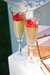 Two wineglasses with champagne and raspberries on wedding ceremony outdoors