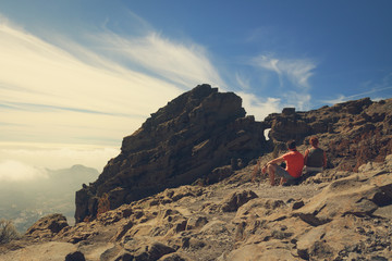 Fototapeta premium Two mature tourists sitting on rocky mountains of Gran Canaria island.