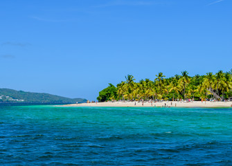 Beautiful beach with palms, blue sky and turquoise ocean, some tourists having fun at the beach, swimming in the ocean, relaxing, Caribbean sea