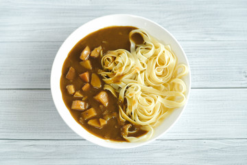 Fusion Japanese curry with pasta, potatoes and carrots on the white wooden table