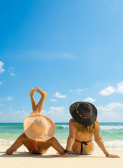 Sexy bikini body of two women enjoy the sea by laying down on sand of beach wearing hat. Happy island lifestyle. White sand and crystal sea of tropical beach.