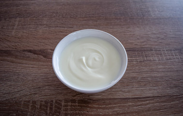 Obraz na płótnie Canvas Ceramic bowl of white yogurt on wooden background from above view, plain yoghurt