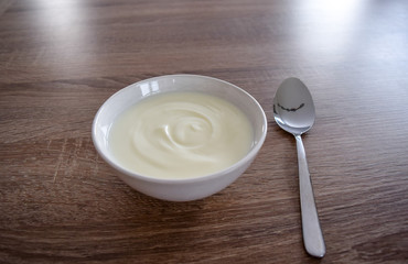Bowl of white yogurt with spoon isolated on vintage rustic wooden table from above, plain yoghurt