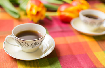 Two small cups of coffee on the saucers on the table with tulips. Meeting for two veterans: May 9 is the day of victory.