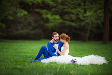 The bride and groom sitting on the grass. A wedding in the summer.