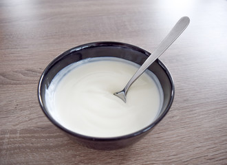 Bowl of white yogurt with spoon isolated on vintage rustic wooden table from above, plain yoghurt